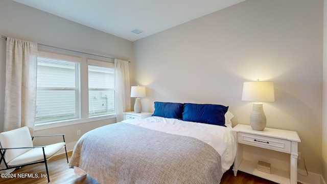 bedroom with baseboards, visible vents, and wood finished floors