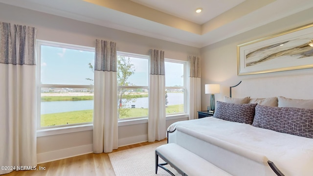 bedroom featuring recessed lighting, a raised ceiling, a water view, wood finished floors, and baseboards