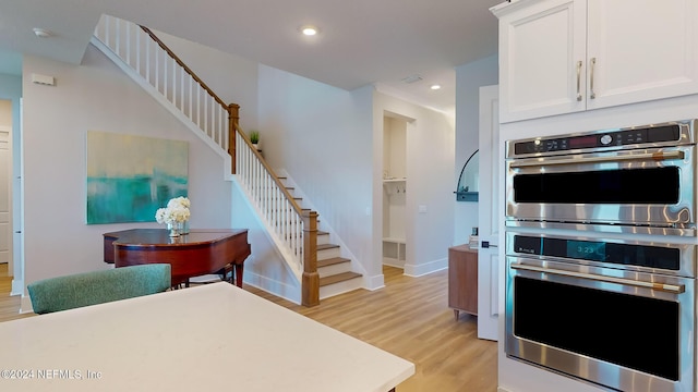 kitchen with recessed lighting, light wood-style flooring, stainless steel double oven, white cabinets, and baseboards