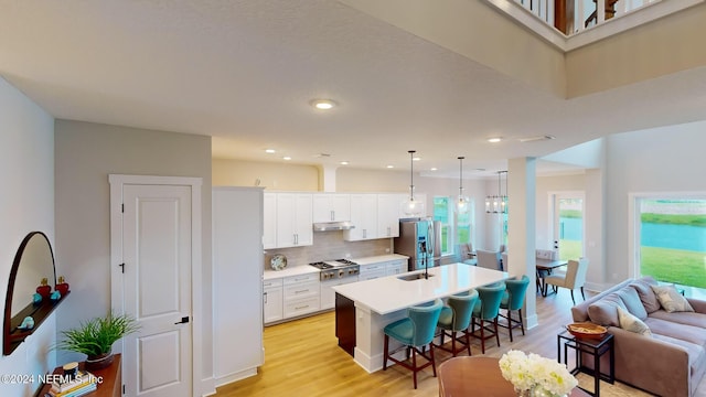 kitchen featuring a kitchen island with sink, under cabinet range hood, white cabinets, a kitchen breakfast bar, and appliances with stainless steel finishes