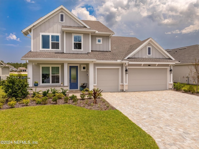 craftsman-style house with decorative driveway, a shingled roof, board and batten siding, a garage, and a front lawn