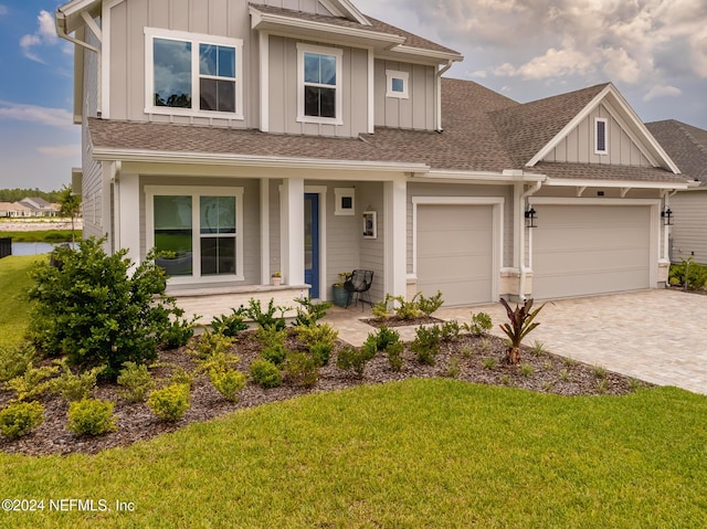 view of front facade featuring decorative driveway, a porch, a shingled roof, board and batten siding, and a front lawn