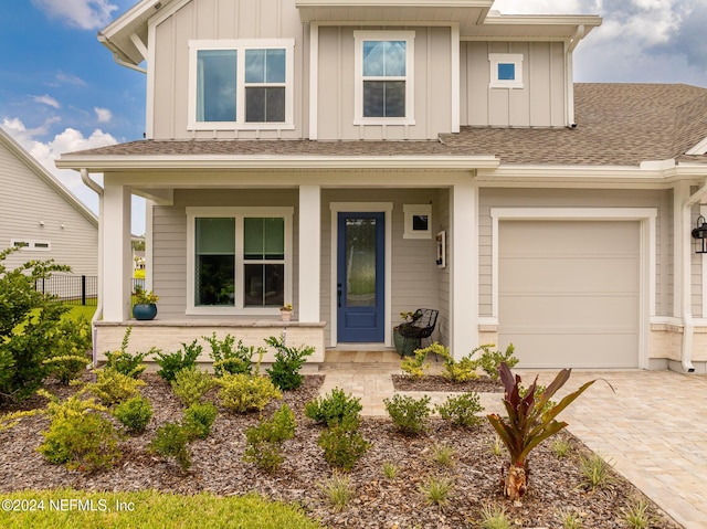 view of front of home featuring decorative driveway, roof with shingles, a porch, board and batten siding, and fence