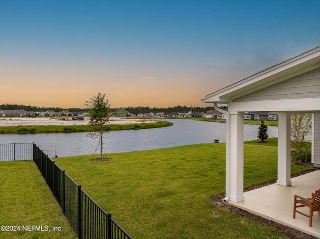 yard at dusk featuring a water view and fence