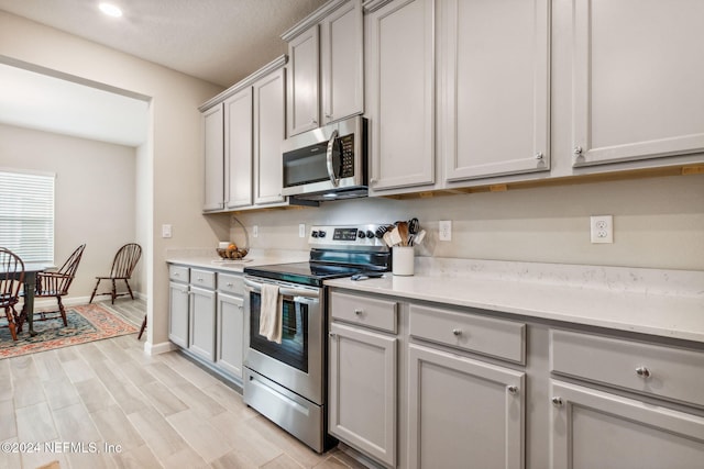 kitchen featuring gray cabinetry, light wood-type flooring, a textured ceiling, and stainless steel appliances