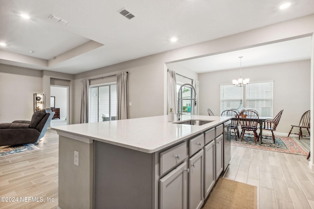 kitchen featuring light hardwood / wood-style floors, dishwasher, hanging light fixtures, sink, and an island with sink