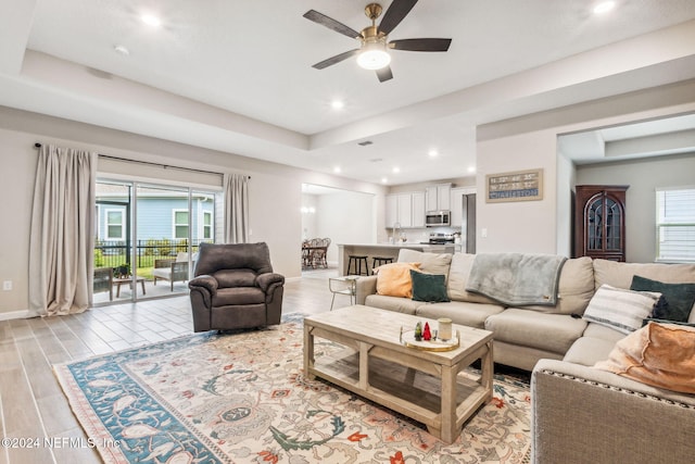 living room with ceiling fan, a raised ceiling, and light hardwood / wood-style flooring