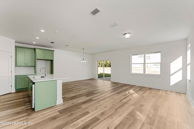 kitchen with sink, an inviting chandelier, green cabinets, light hardwood / wood-style flooring, and a center island with sink