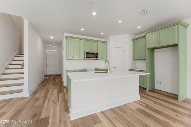 kitchen featuring green cabinets, sink, a kitchen island with sink, and light hardwood / wood-style flooring