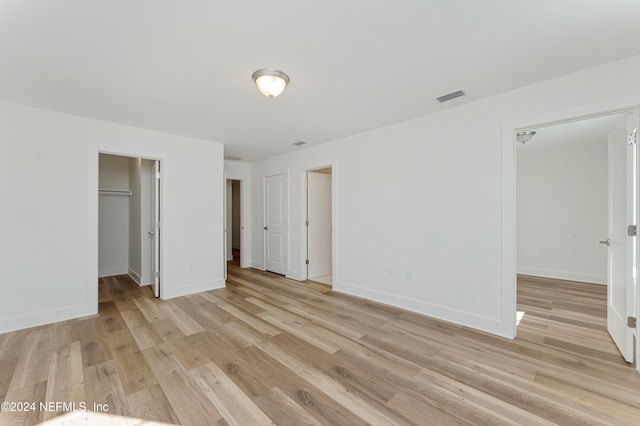 unfurnished bedroom with a spacious closet, a closet, and light hardwood / wood-style floors