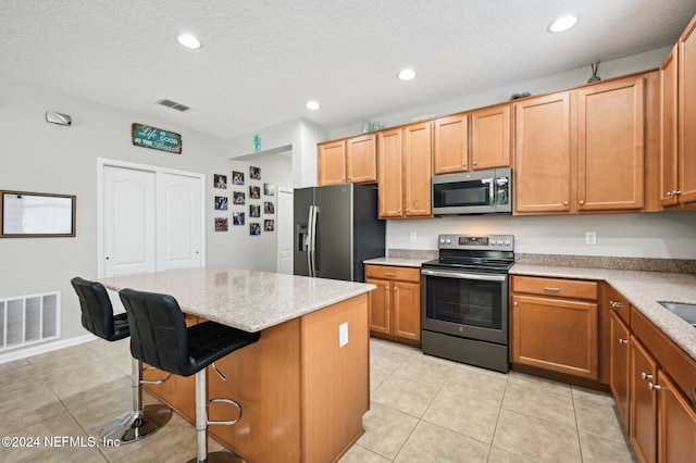 kitchen featuring stainless steel appliances, a kitchen island, a textured ceiling, a kitchen bar, and light tile patterned floors