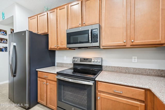 kitchen featuring light tile patterned flooring, light stone countertops, and stainless steel appliances