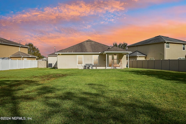 back house at dusk with a lawn and a patio area