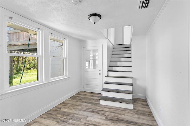 staircase featuring crown molding, a textured ceiling, and hardwood / wood-style flooring