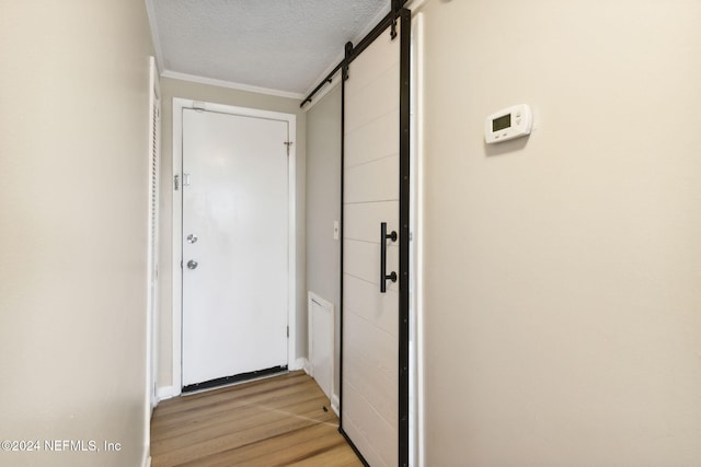 doorway to outside with light wood-type flooring, a barn door, crown molding, and a textured ceiling