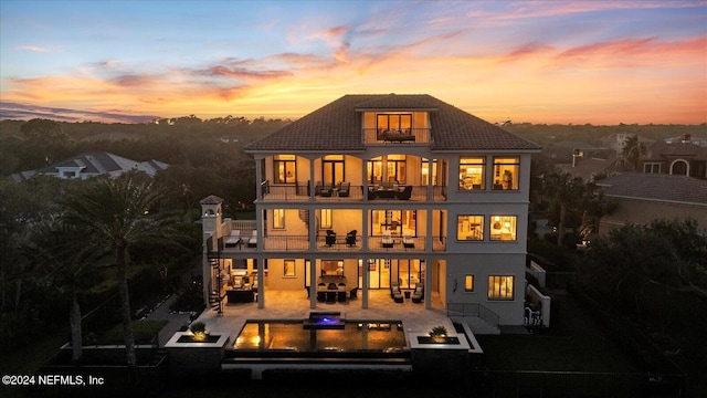 back house at dusk with a balcony, outdoor lounge area, a patio, and a hot tub