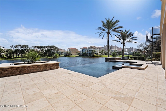 view of pool featuring an in ground hot tub, a water view, and a patio area