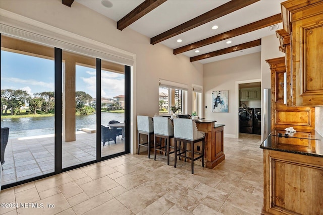 kitchen with a water view, a kitchen breakfast bar, dark stone counters, beam ceiling, and washer and dryer