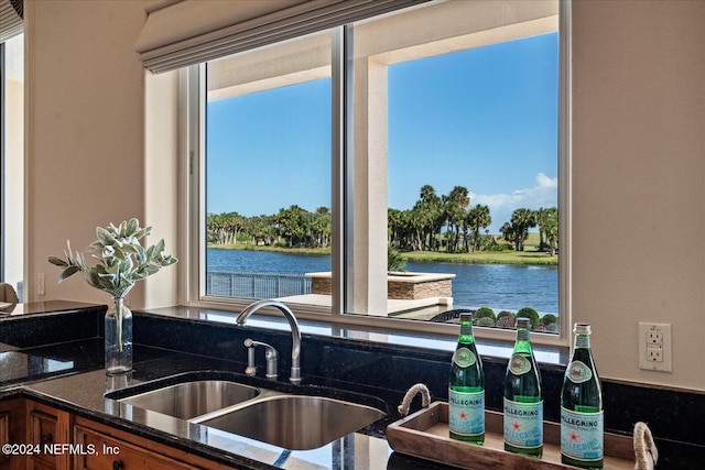 kitchen with dark stone counters, a water view, and sink