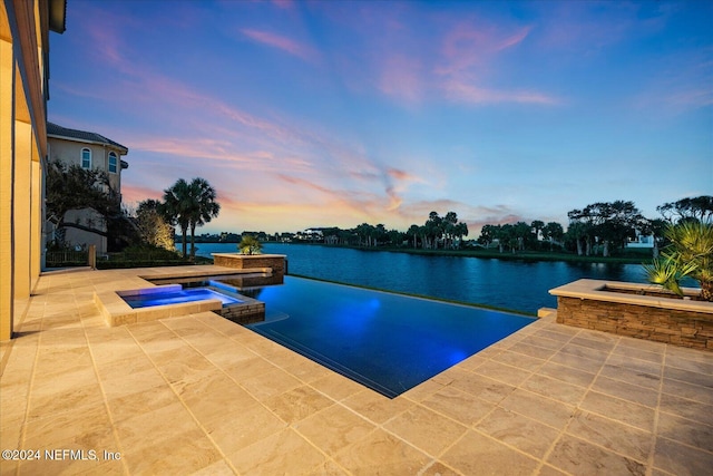 pool at dusk featuring a patio, a water view, and an in ground hot tub