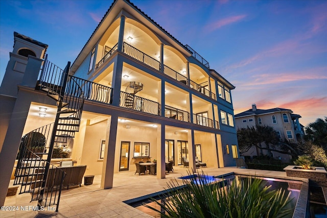 back house at dusk featuring a patio area, ceiling fan, and a balcony