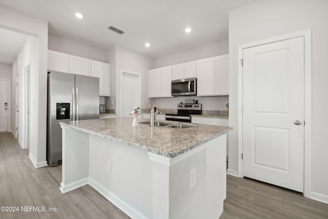 kitchen with appliances with stainless steel finishes, light stone counters, a center island with sink, white cabinets, and light hardwood / wood-style floors