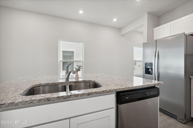 kitchen with sink, light wood-type flooring, appliances with stainless steel finishes, light stone counters, and white cabinetry