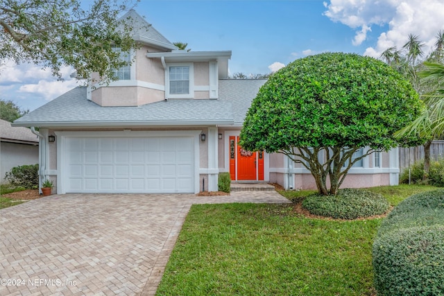 view of front of property with roof with shingles, a front yard, decorative driveway, and stucco siding