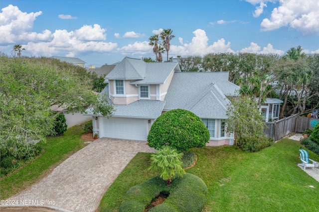 traditional home with a garage, decorative driveway, roof with shingles, and fence