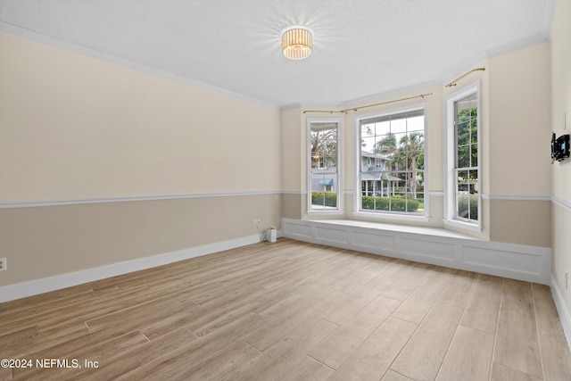 unfurnished room featuring baseboards, a textured ceiling, light wood-type flooring, and crown molding