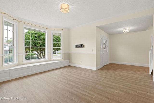 interior space featuring light wood finished floors, baseboards, ornamental molding, a textured ceiling, and a decorative wall