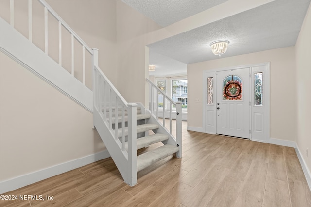 foyer entrance with light wood finished floors, stairs, and baseboards