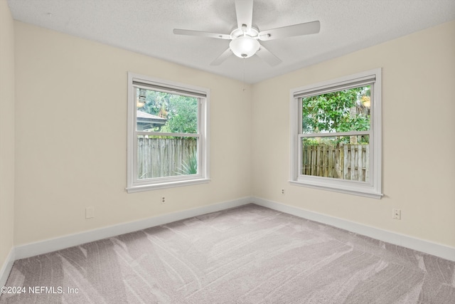 spare room with light carpet, a ceiling fan, baseboards, and a textured ceiling