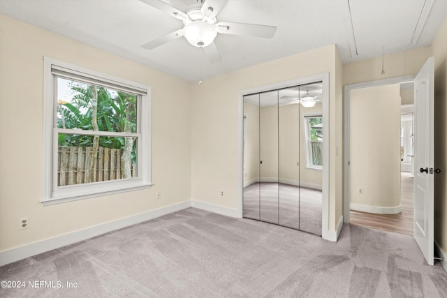 unfurnished bedroom with a closet, attic access, light carpet, ceiling fan, and baseboards