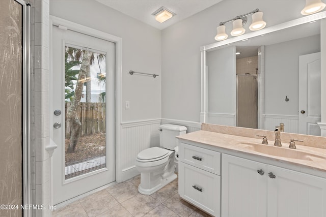 bathroom featuring a shower with door, toilet, wainscoting, vanity, and tile patterned floors