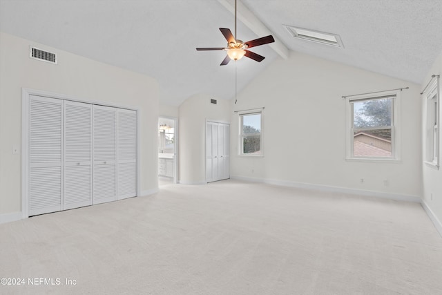 unfurnished bedroom with multiple windows, visible vents, beam ceiling, and light colored carpet