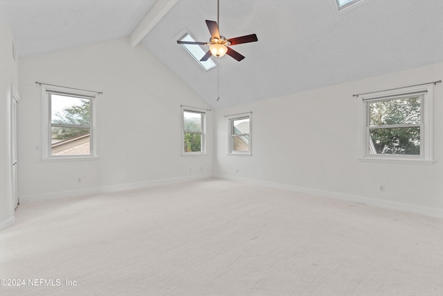 spare room with ceiling fan, light carpet, a skylight, baseboards, and beamed ceiling