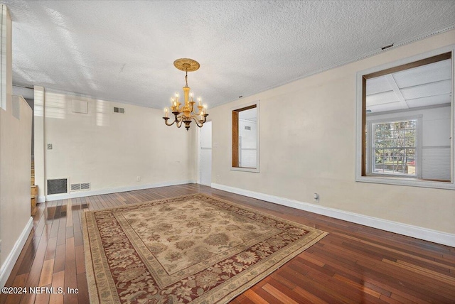 empty room with hardwood / wood-style floors, a textured ceiling, and an inviting chandelier