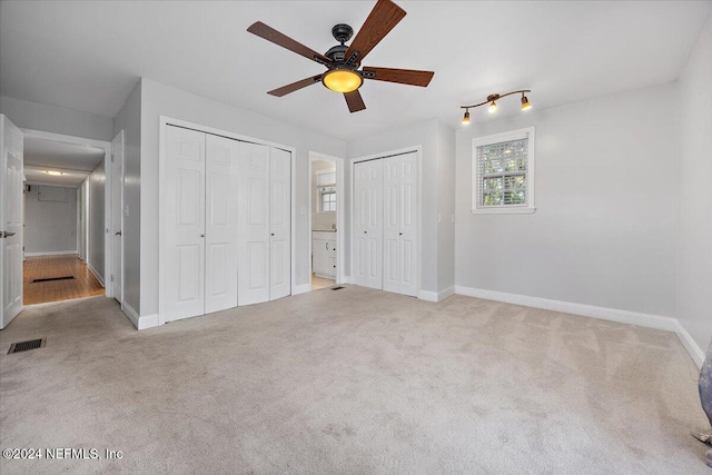 unfurnished bedroom featuring light colored carpet, ceiling fan, and multiple closets