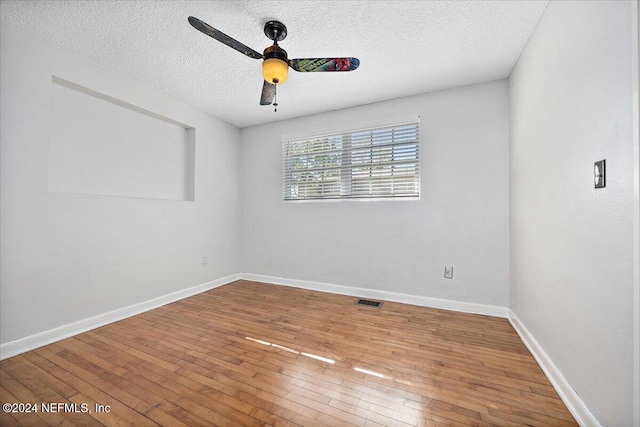 empty room with ceiling fan, wood-type flooring, and a textured ceiling