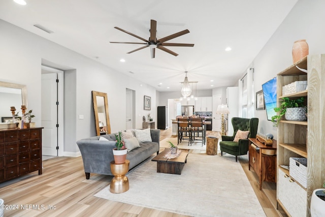 living room with ceiling fan with notable chandelier and light hardwood / wood-style floors