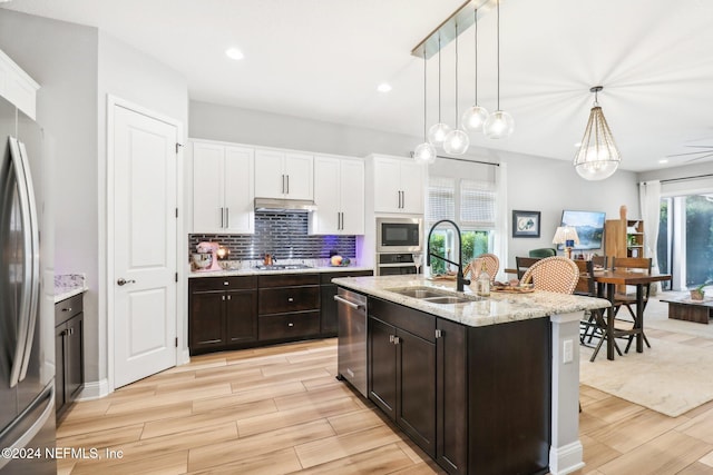 kitchen featuring stainless steel appliances, sink, light hardwood / wood-style flooring, hanging light fixtures, and an island with sink