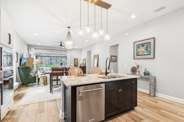 kitchen with a center island with sink, sink, light stone countertops, decorative light fixtures, and light hardwood / wood-style floors