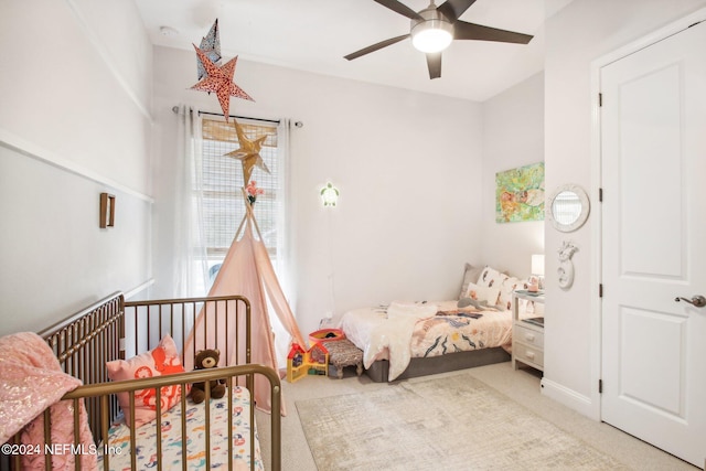 carpeted bedroom with ceiling fan and a nursery area