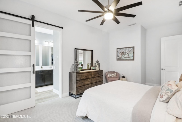 bedroom featuring a barn door, ensuite bathroom, and ceiling fan