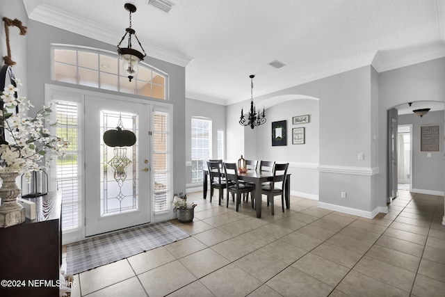 tiled foyer entrance featuring a textured ceiling, ornamental molding, and a notable chandelier