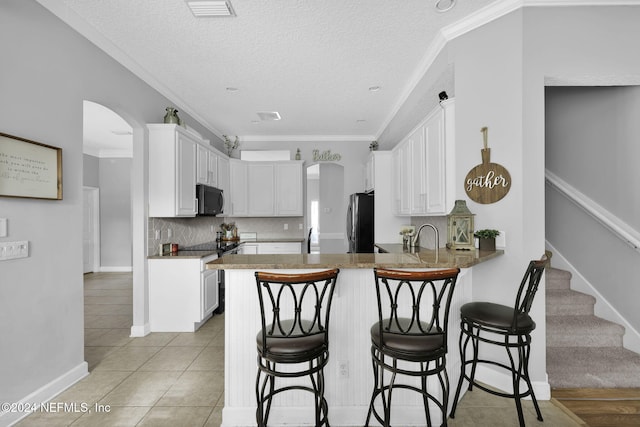 kitchen with kitchen peninsula, white cabinets, stainless steel appliances, and ornamental molding