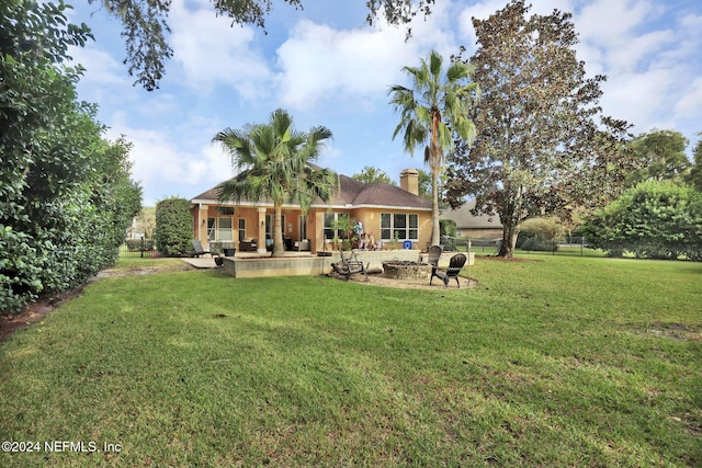 rear view of property featuring a yard, a patio, and an outdoor fire pit