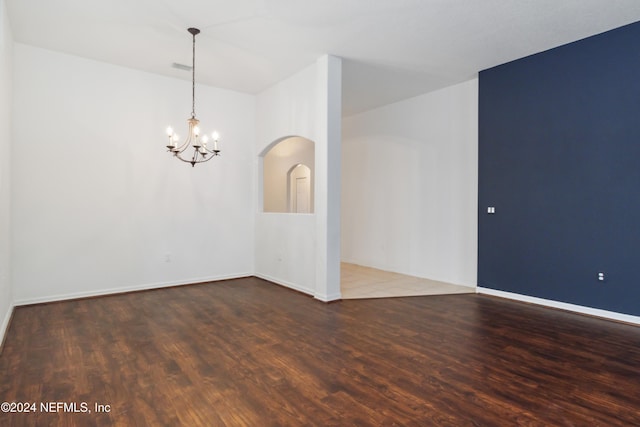 spare room featuring a chandelier, wood finished floors, baseboards, and arched walkways