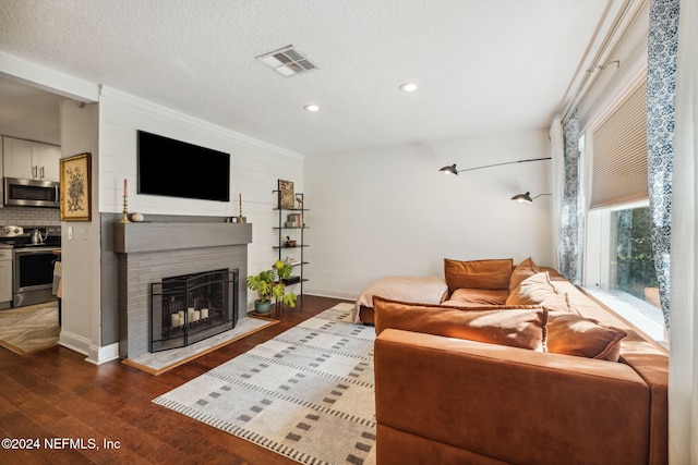 living room with a textured ceiling, dark hardwood / wood-style flooring, a brick fireplace, and crown molding